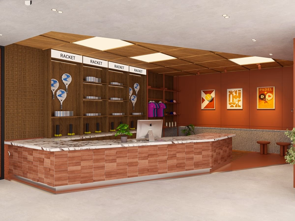 The pro shop wall — lit racket displays and stock shelving in timber, framed padel posters beyond