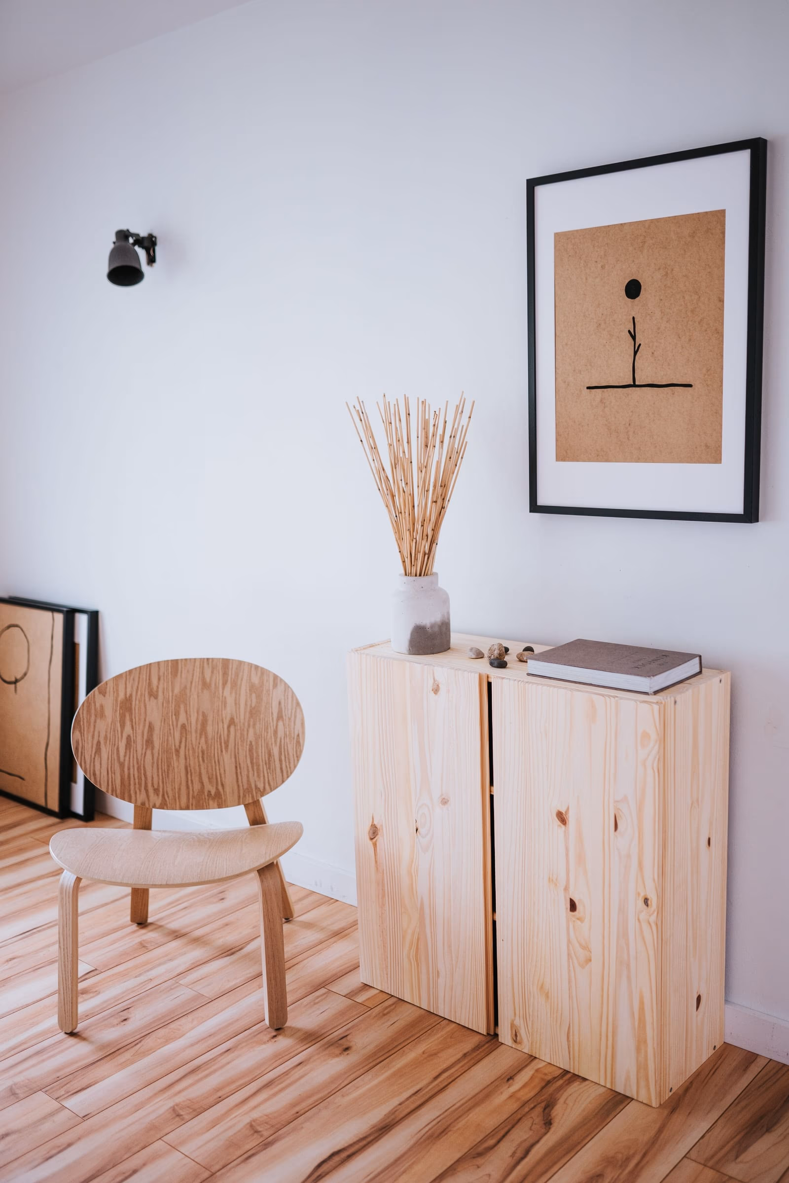 Styled vignette of a framed print, dried grasses and a pale timber cabinet