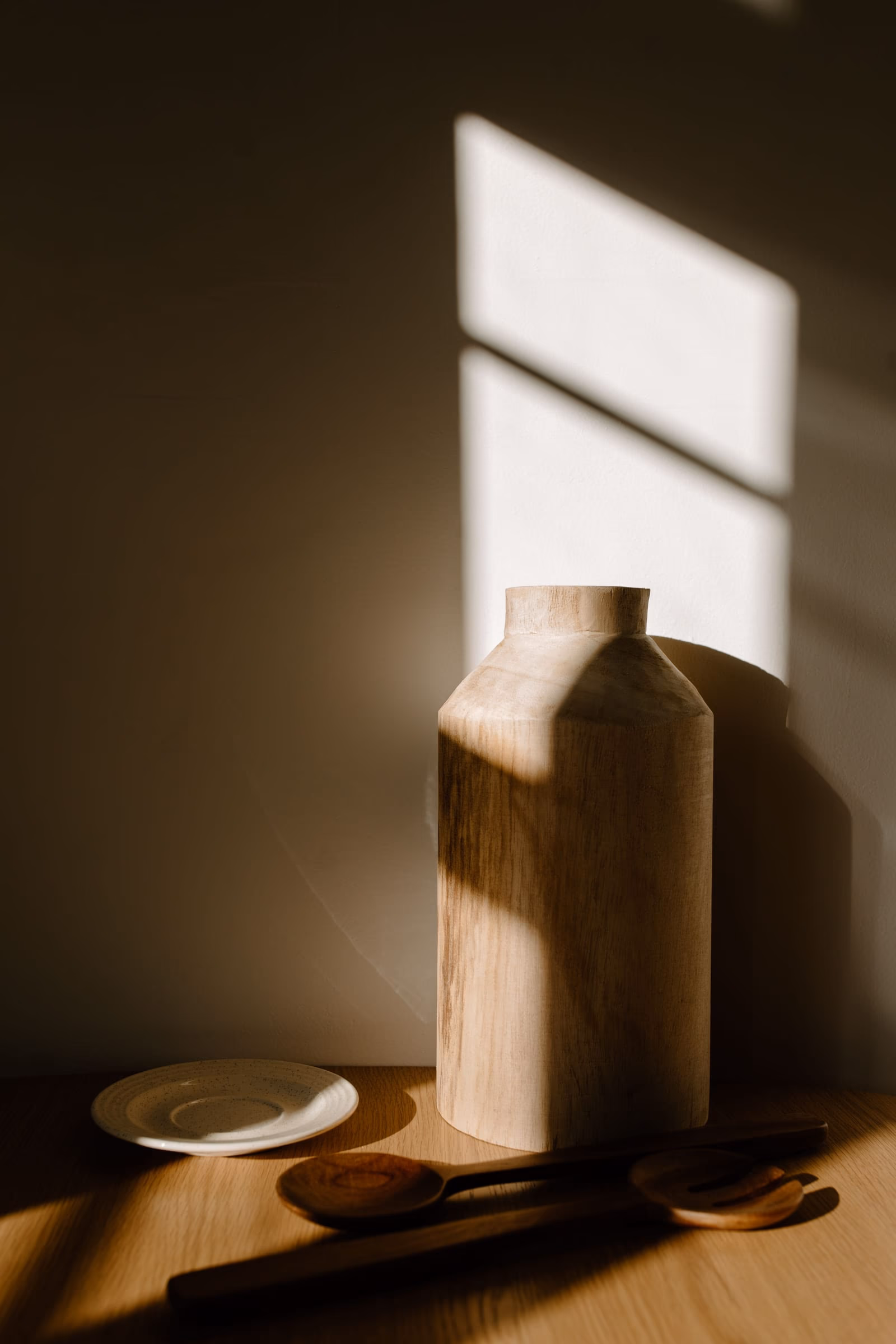 Turned timber vessels and a shallow plate on a bare table, held in low light